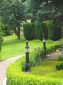 Light-Bollard, Abbildung Die Lichtpoller stehen auf kleinen Fundamenten hinter der Hecke. Ausführung der Poller in Schwarz, Kupfer und Gold Patina.
