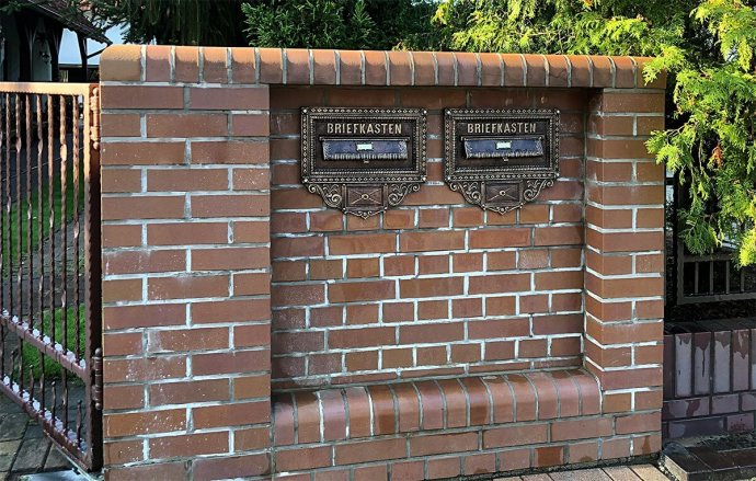 Zwei Briefeinwurfplatten (Art. 1520) hier in der Sonderausführung mit einem Namenschildchen auf der Einwurfklappe und einem Klingelknopf unten im rechteckigen Brieffeld. Lackierung in Schwarz, Kupfer & Gold Patina.